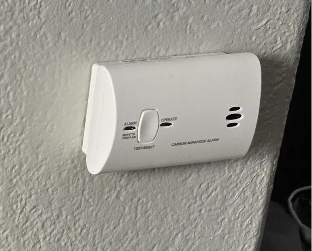 A hand pressing the test button on a wall CO alarm
